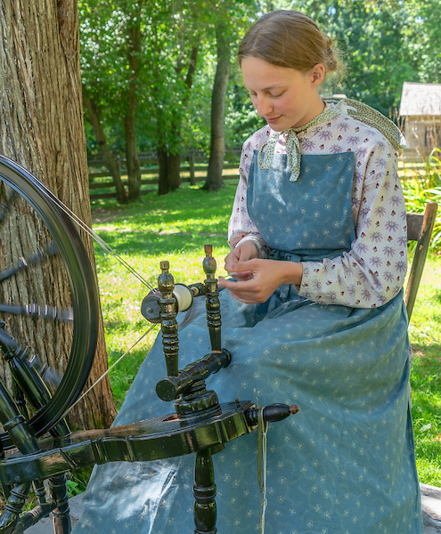 Someone dressed in period time clothing spinning wool